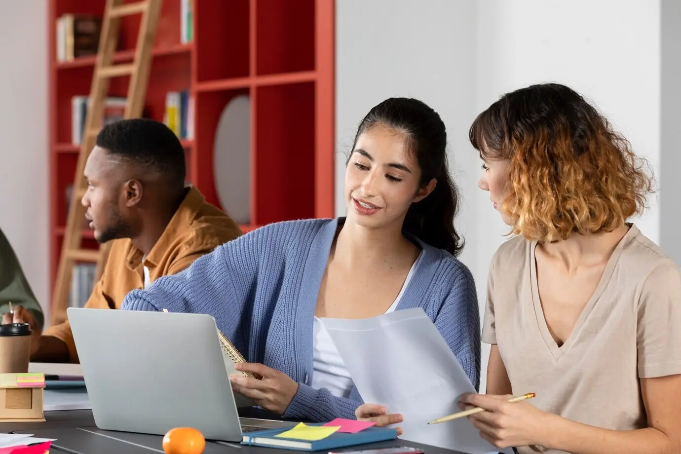 Eine junge Frau zeigt einer Freundin oder einem Freund während einer Lernsitzung ihre Notizen.